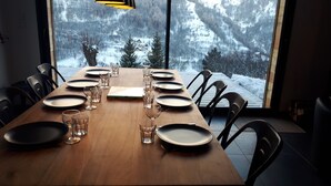Une table à manger dressée pour 10 personnes, avec assiettes, verres et couverts, donnant sur un paysage montagneux enneigé.