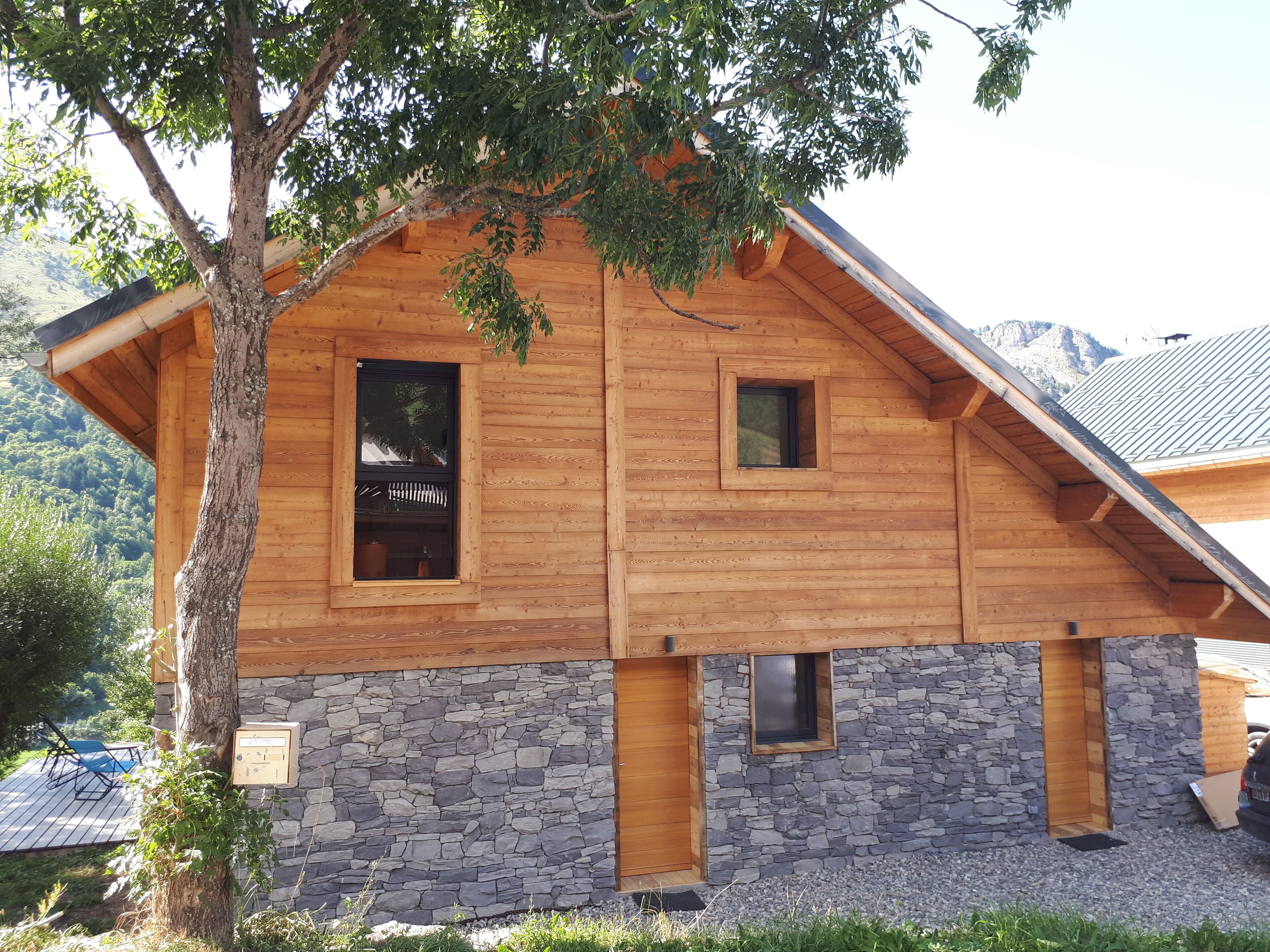 A wooden cabin with stone foundation, two windows, and a tree in front.