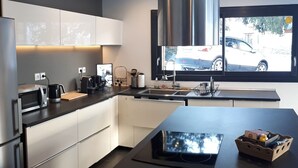 Une cuisine moderne dotée d’appareils électroménagers en acier inoxydable, d’un grand îlot central et d’une fenêtre donnant sur une voiture garée.