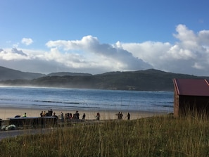 A beach with people, a small building, and hills in the background.