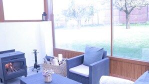 A cozy outdoor seating area with wicker furniture, a fireplace, and a view of a fenced yard. - House in a natural setting, 200m from the beach in Costa da Morte (Balarés)