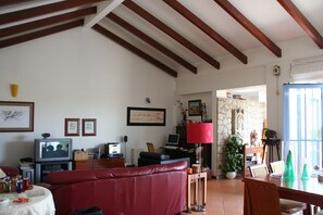 A living room with a red sofa, a television, a dining table, and a stone wall.