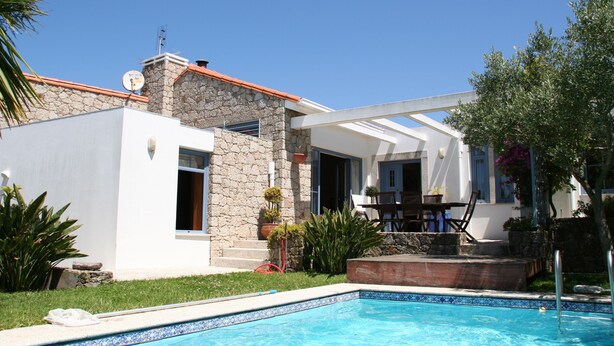 A modern house with a swimming pool, stone exterior, and a patio area with outdoor furniture.
