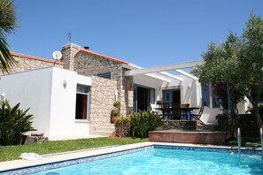 Ein modernes Haus mit Swimmingpool, Natursteinfassade und einer Terrasse mit Gartenmöbeln.
