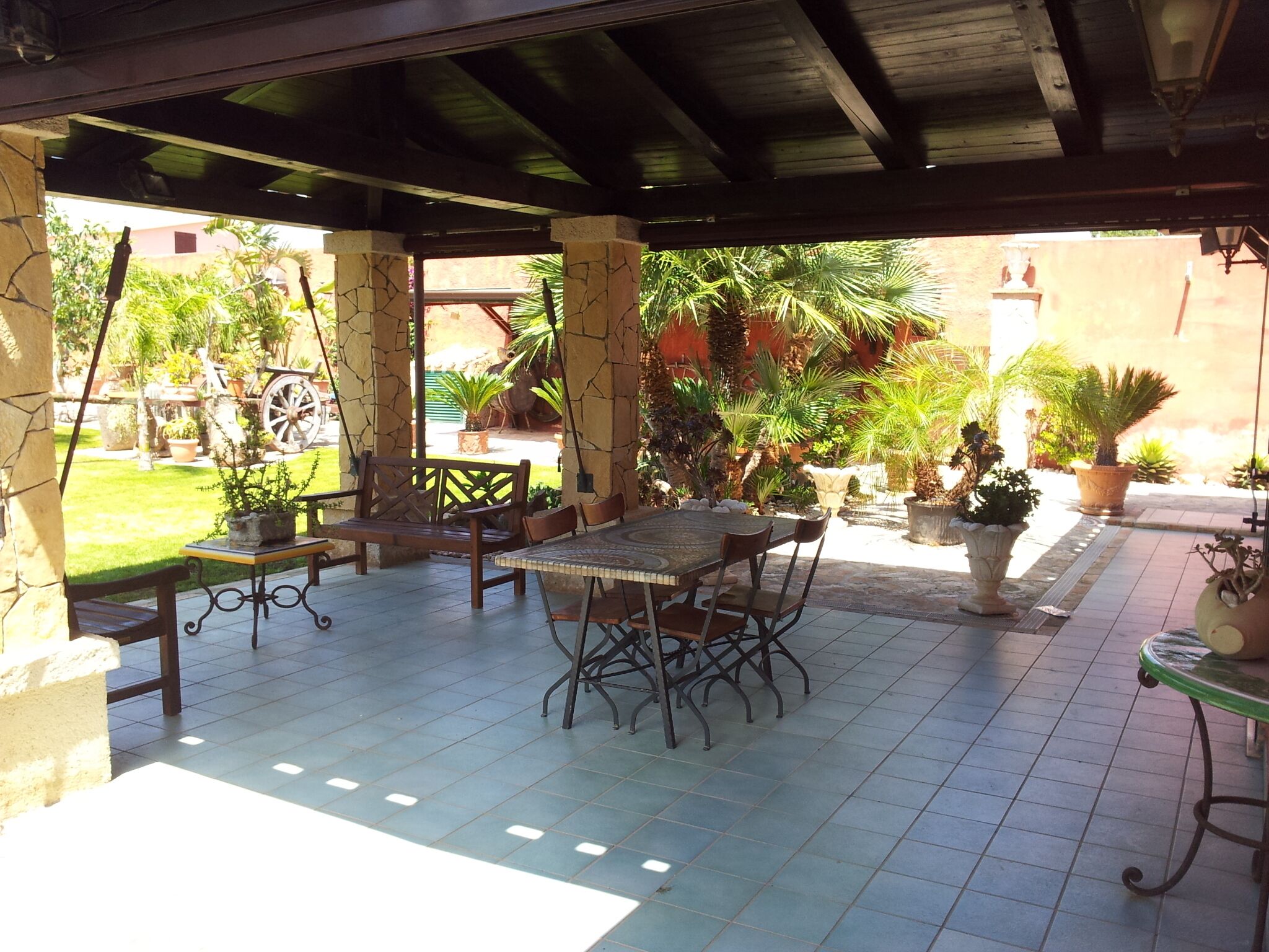 Eine Terrasse im Freien mit gefliestem Boden, einem Holztisch mit Stühlen und Topfpflanzen.