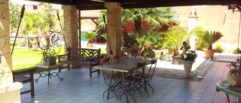 Eine Terrasse im Freien mit gefliestem Boden, einem Holztisch mit Stühlen und Topfpflanzen.