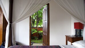 A bedroom with a bed, a nightstand, a red lamp, and a view of a garden through an open door. - Typical Balinese villa with beautifully landscaped swimming pool (Buleleng)