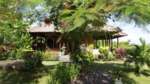 A thatched-roof pavilion surrounded by lush greenery and flowering plants. - Typical Balinese villa with beautifully landscaped swimming pool (Buleleng)