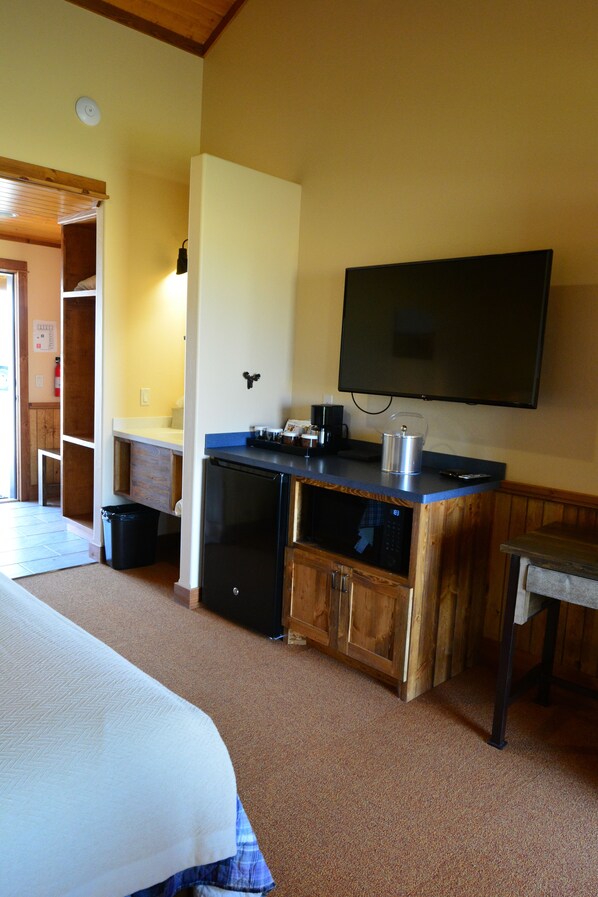 Habitación de hotel con cama, escritorio, televisión de pantalla plana, cafetera y cubo de basura.