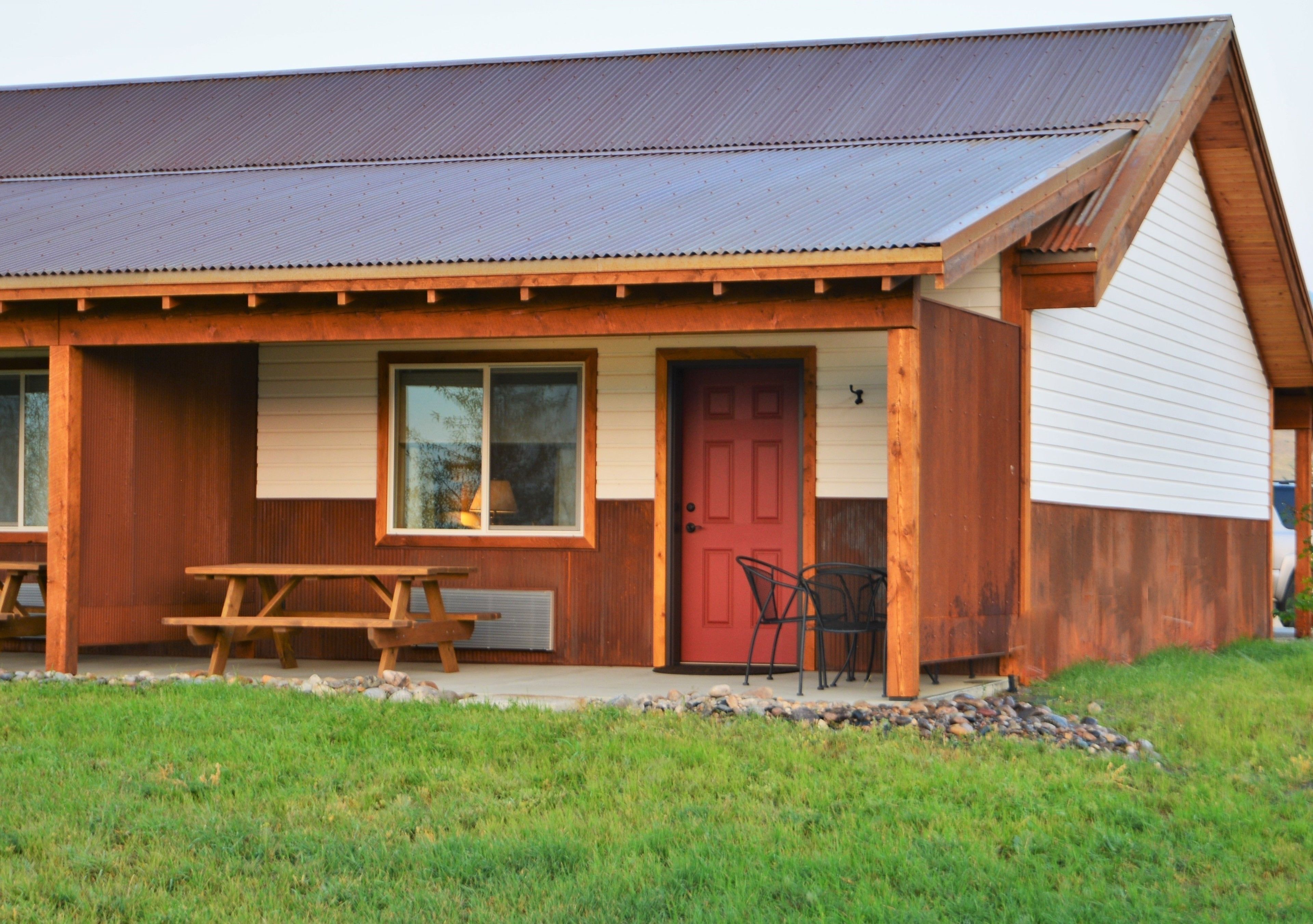 A wooden building with a red door, a large window, and a picnic table outside.