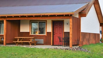 A wooden building with a red door, a large window, and a picnic table outside.