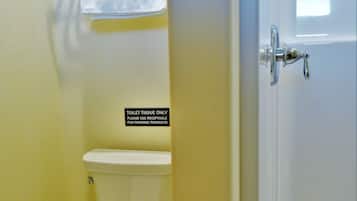 A bathroom with a toilet, a towel rack, and a sign indicating the use of toilet tissue for feminine products.