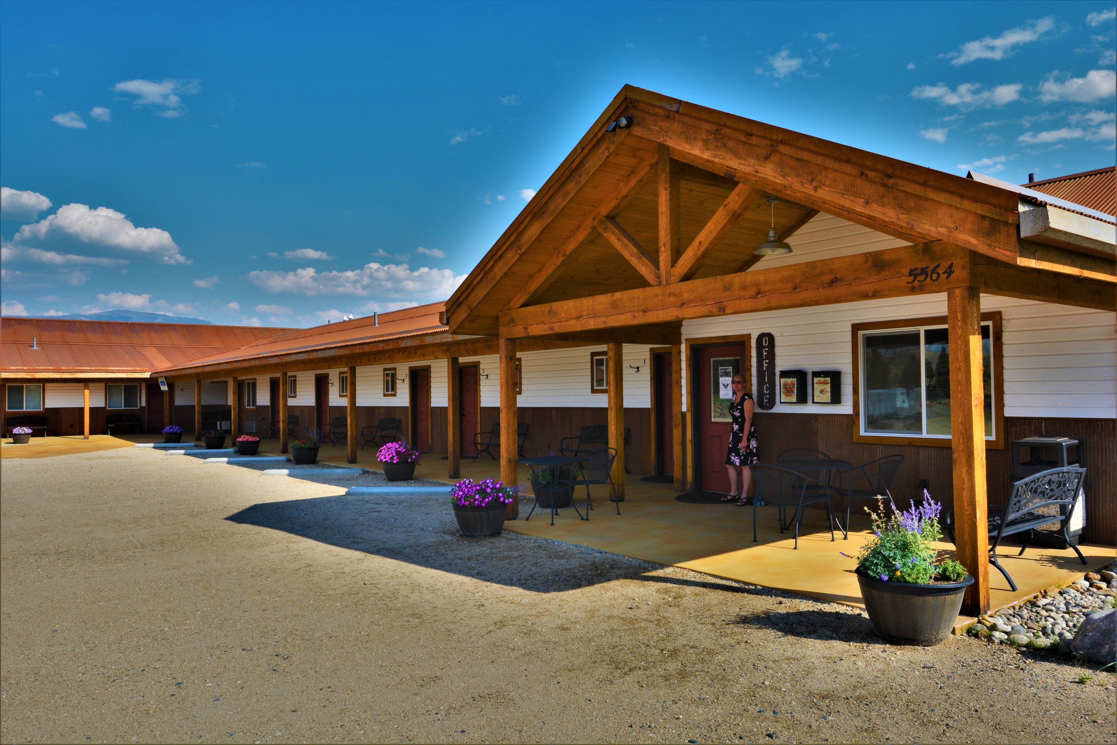 Un motel con un área de estar al aire libre cubierta, varias habitaciones y un camino de entrada de grava.