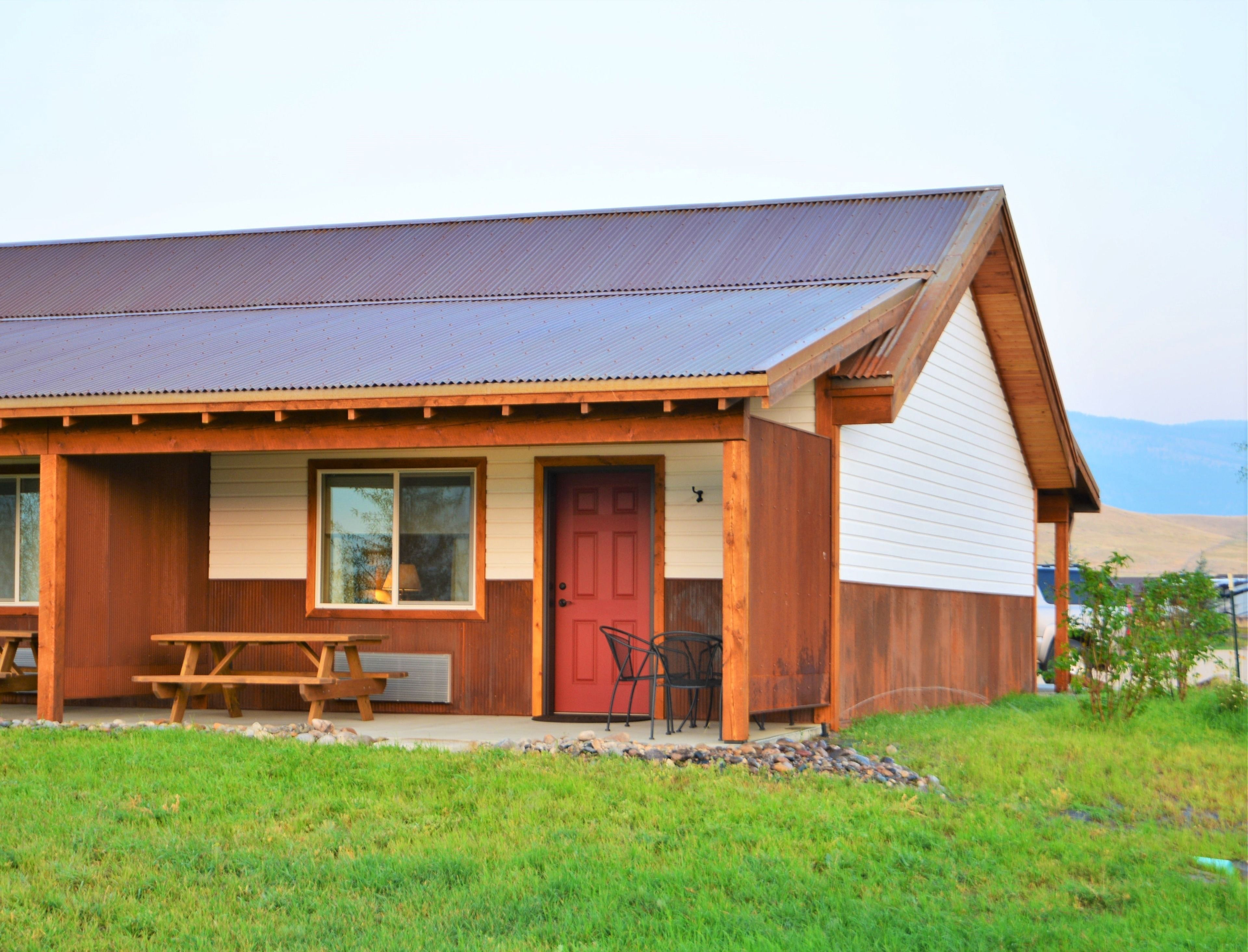 A rustic wooden cabin with a red door, a picnic table, and a covered patio area.