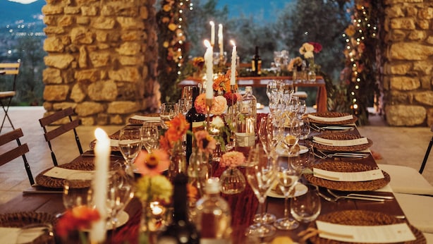 An outdoor dining setup with stone pillars, string lights, and a view of mountains.