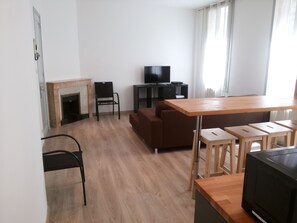 A modern living room with a fireplace, a sofa, a TV, and a wooden dining table with stools. - T3 renovated near the clock square, in the heart of the historic center (Avignon)