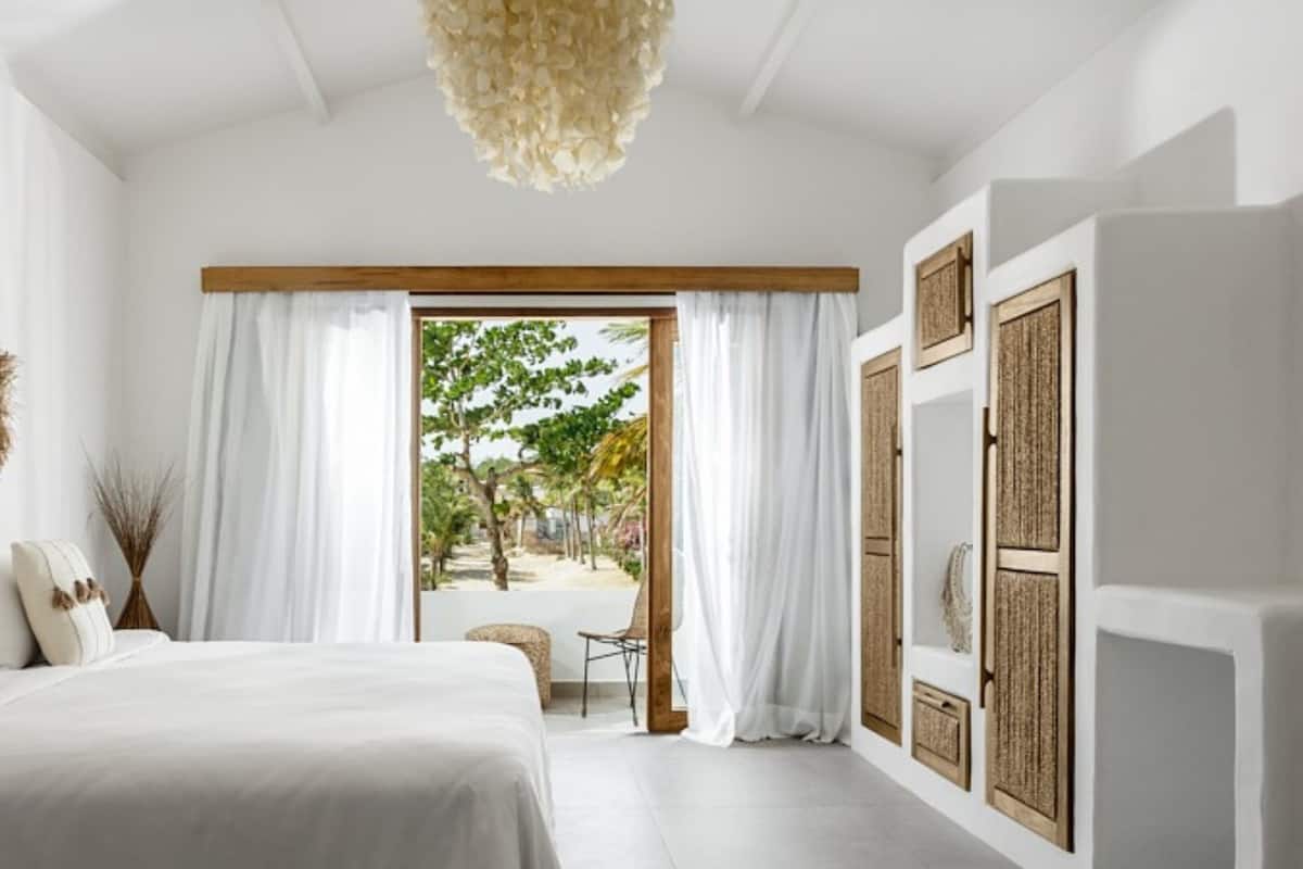 A modern bedroom with a large bed, a view of a garden through a sliding door, and a ceiling light fixture.