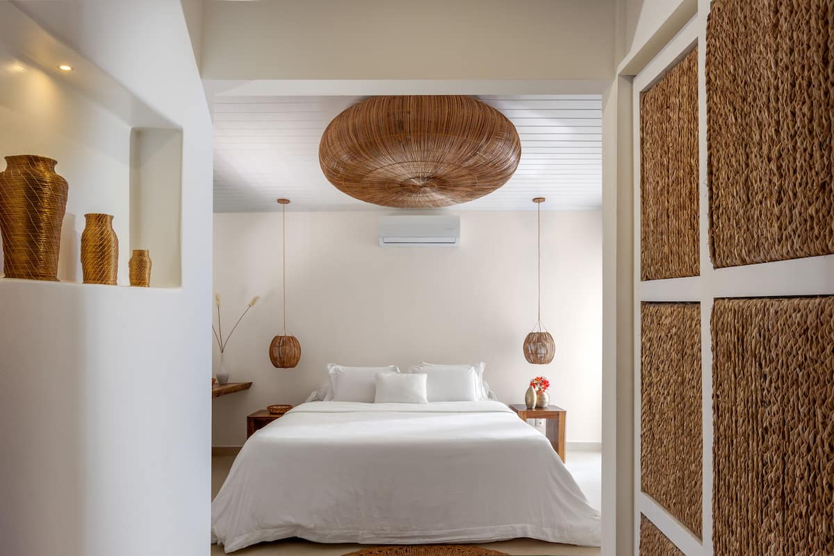 A modern bedroom with a large bed, a hanging woven light fixture, and a wall-mounted air conditioner.