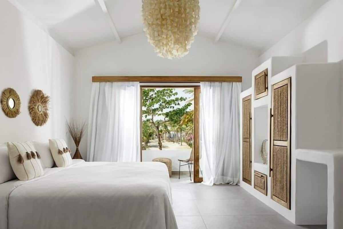 A bedroom with a bed, curtains, a view of the outdoors, and a ceiling light fixture.