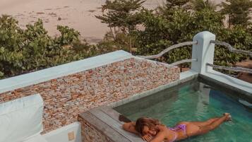 A pool area with a person relaxing, surrounded by a beach view and palm trees.