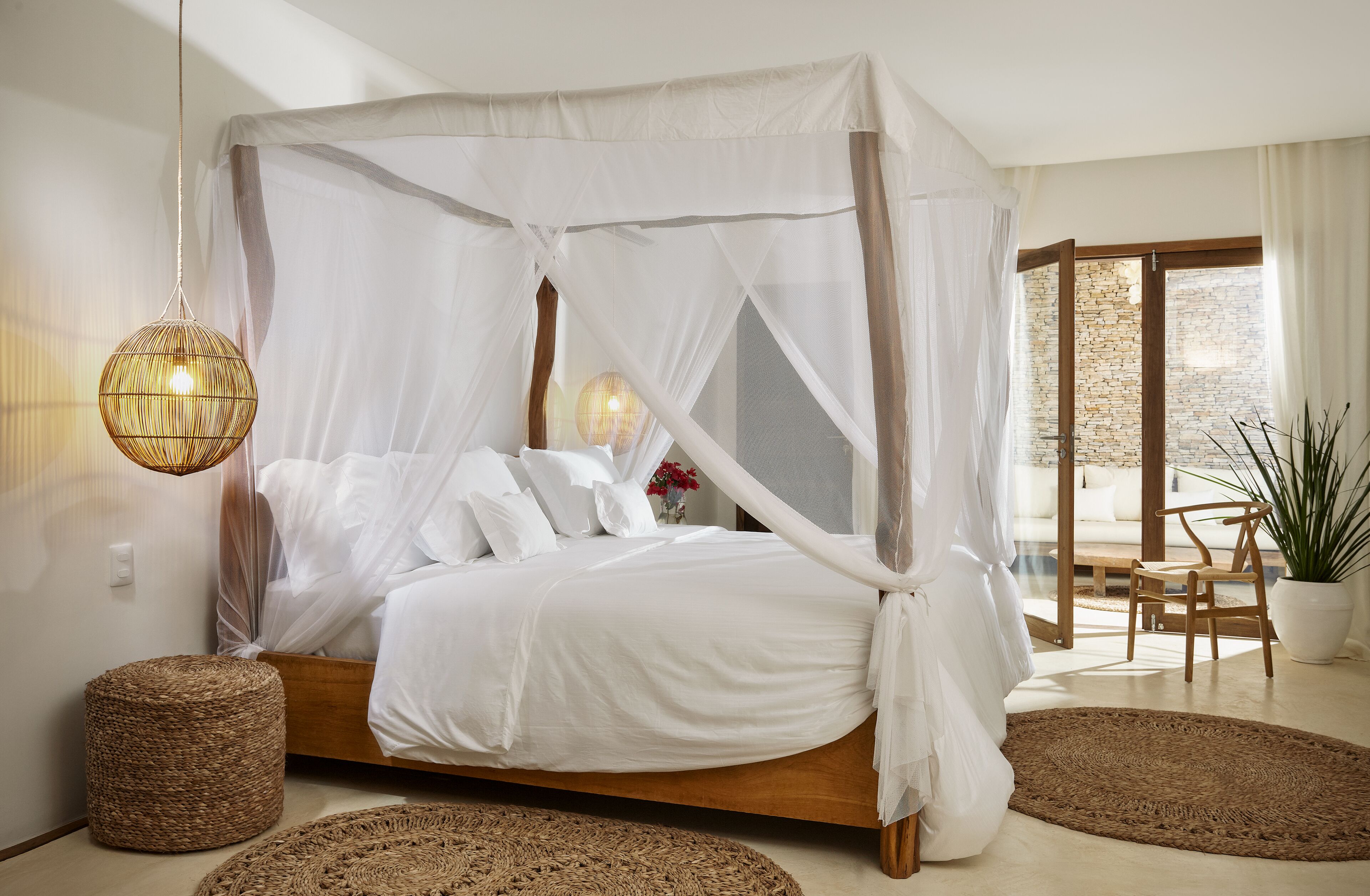 A bedroom with a canopy bed, wicker ottomans, and a view of the outdoors.