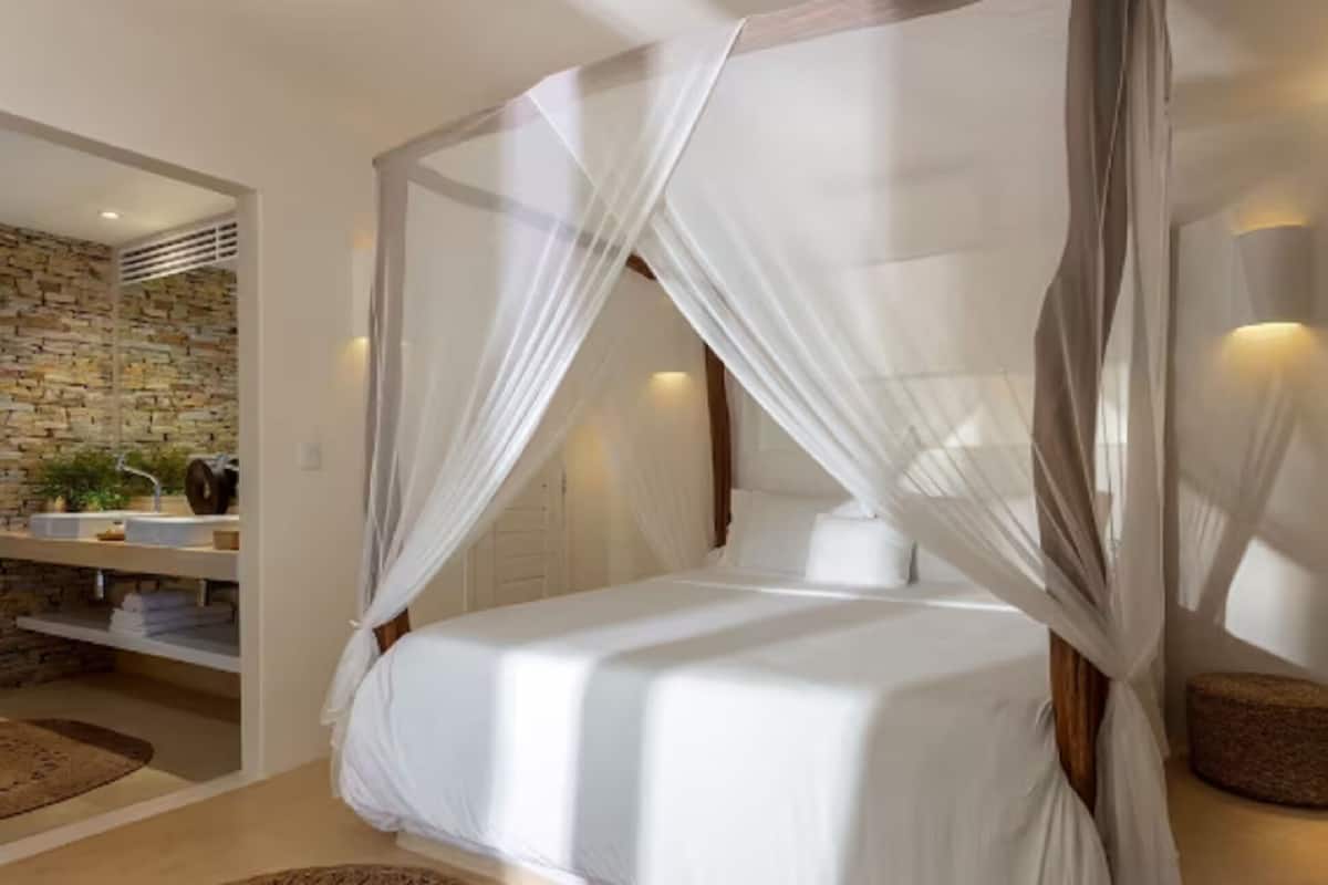A bedroom with a four-poster bed, a stone wall, a sink, and a small stool.