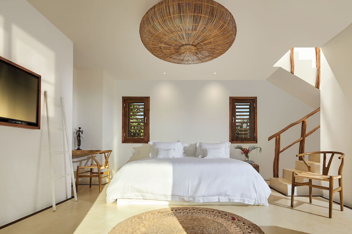 A bedroom with a large bed, a TV, a wooden chair, and a staircase.