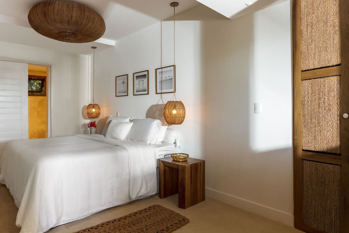 A bedroom with a bed, two bedside tables, a hanging light fixture, and framed pictures on the wall.