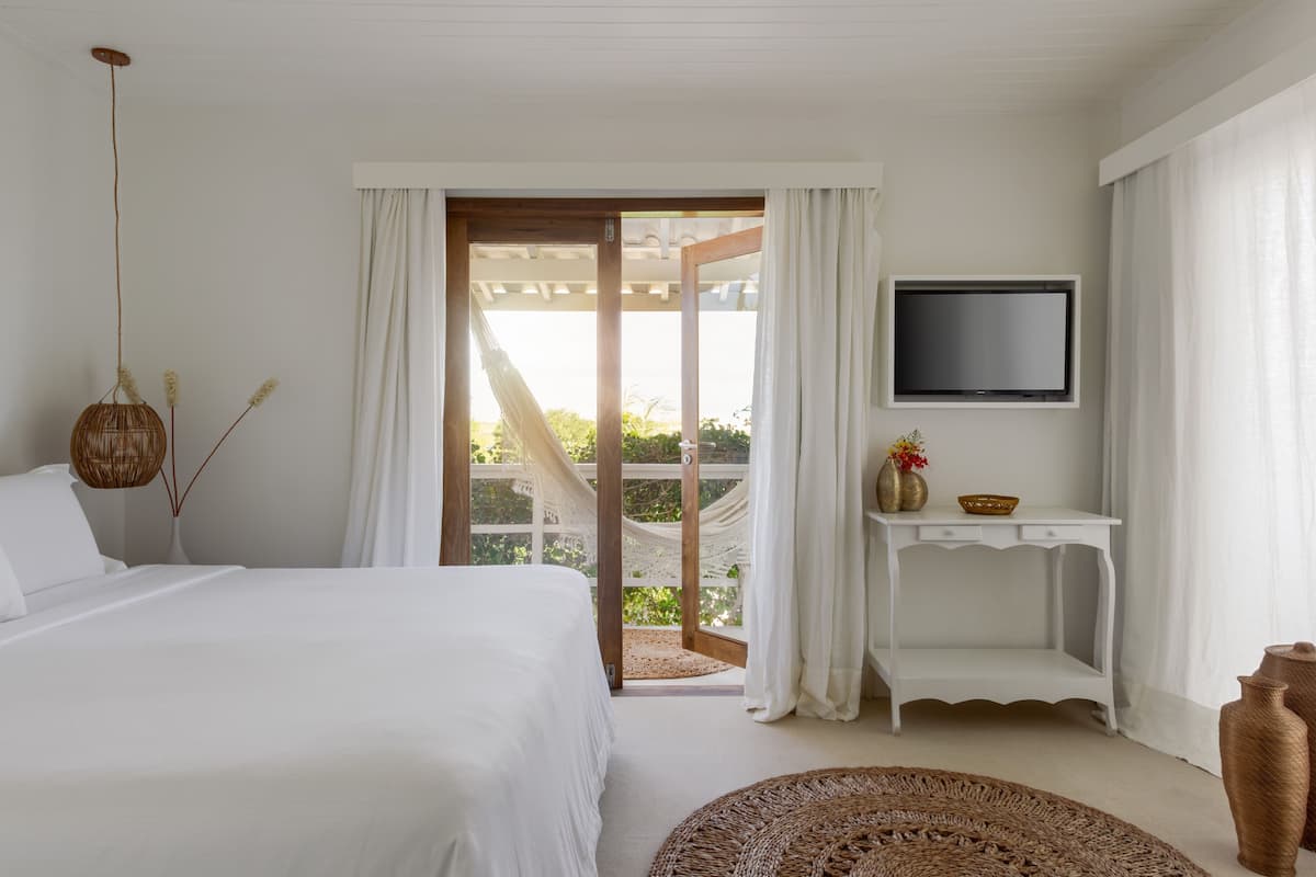 A bedroom with a bed, a TV mounted on the wall, a small table with a vase, and a view of the outdoors through a door.