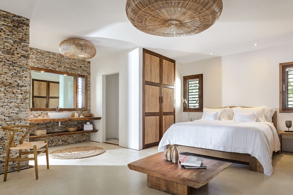 A bedroom with a stone wall, wooden bed, and a large woven light fixture.