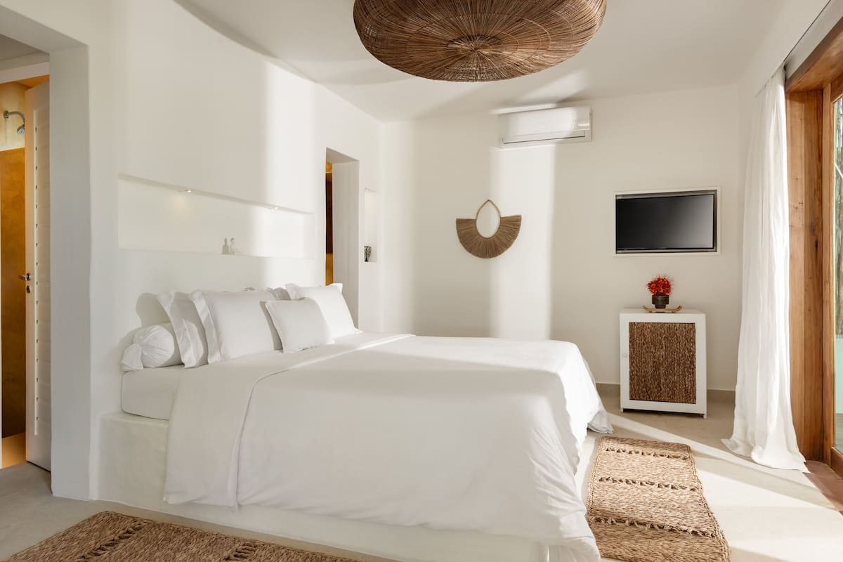 A modern bedroom with a large bed, a TV, a wall-mounted mirror, and a small cabinet.