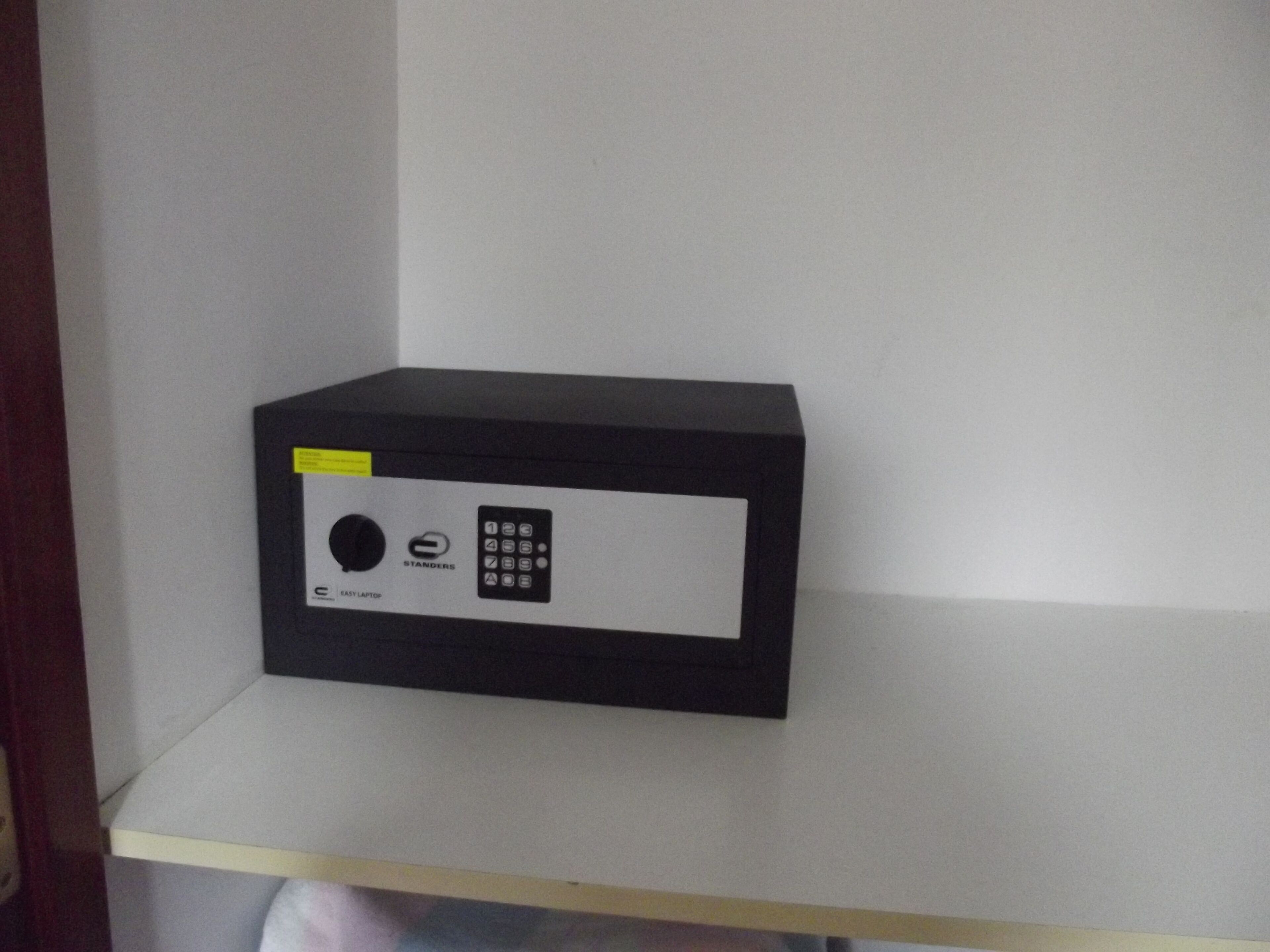 Een zwarte kluis met een keypad en een rond slot op een wit schap.