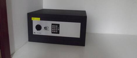Een zwarte kluis met een keypad en een rond slot op een wit schap.