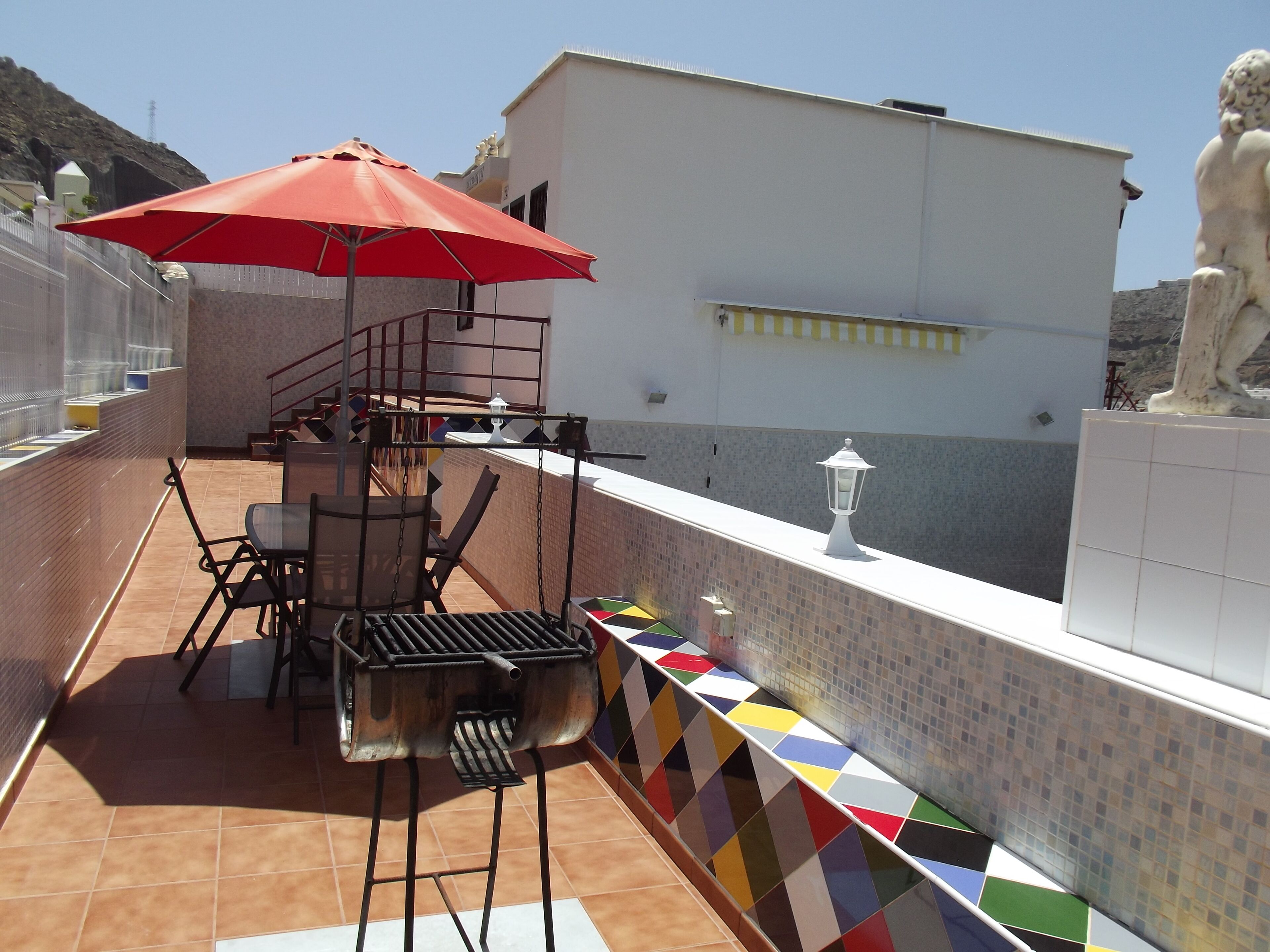 Une terrasse sur le toit équipée d’un barbecue, de chaises et d’un parasol rouge.