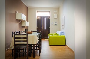 Uma área de refeições com mesa e cadeiras, um sofá verde e piso de madeira.