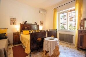 A bedroom with a bed, bedside tables, a window with curtains, a radiator, and a small table with a plate.