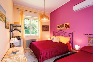A bedroom with two beds, a radiator, a window with curtains, a lamp, and artwork on the walls. - A Villa Offering Comfort and Relaxation Between Mount Etna and the Sea (Zafferana Etnea)