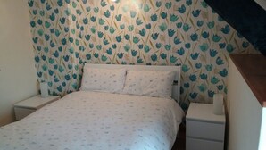 A small, neatly made bed in a room with floral wallpaper. There are two bedside tables, one on each side of the bed.