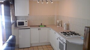 A compact kitchen with white cabinets, a microwave, a gas stove, and a coffee maker.