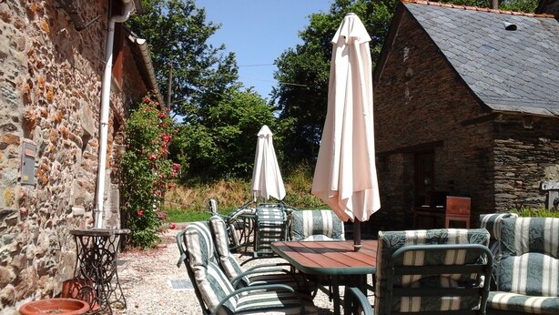 An outdoor seating area with a stone wall, a wooden table, and striped chairs.
