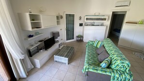 Un soggiorno con divano, televisore e mobili bianchi.