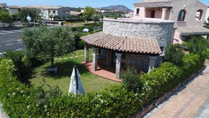 Un edificio in pietra con tetto in tegole, circondato dal verde e da un'area pavimentata.
