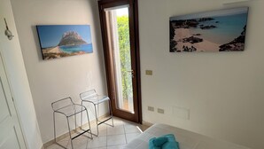 Una stanza con un letto, due sedie trasparenti, una porta che dà su un balcone e due quadri appesi alle pareti.