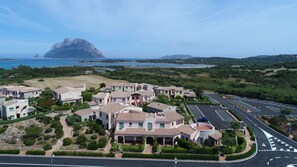 A coastal residential area with villas, a parking lot, and a view of the sea and mountains.