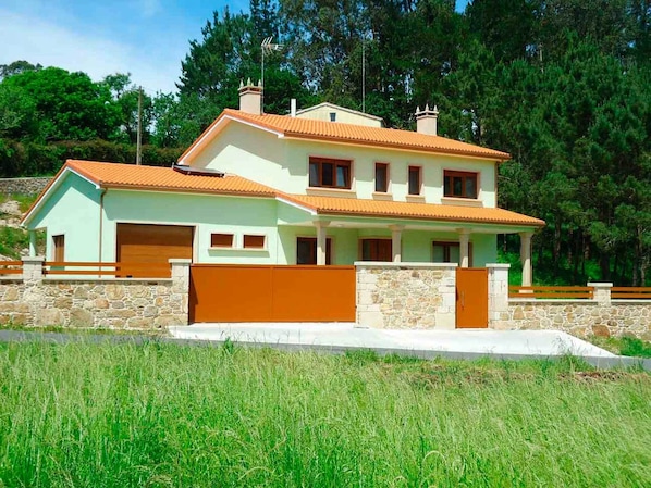 A two-story house with a stone foundation, a tiled roof, and a fenced driveway.