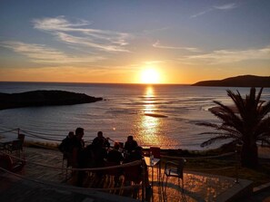 A sunset view from a terrace with a dining area overlooking the sea.