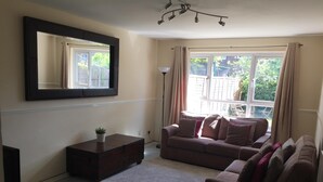 Een woonkamer met een bank, een salontafel, een televisie en een groot raam met gordijnen.