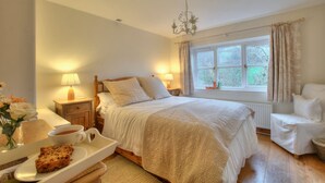 A bedroom with a bed, bedside lamps, a window with curtains, a chair, a tray with a cup and a pastry, and a vase with flowers. - Pretty Stone Cottage: Hot Tub, Real Fire, Wifi & Riverside Views (Pont-faen)