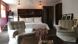 A cozy living room with a bed, two armchairs, a coffee table with books, a ceiling fan, and a bookshelf filled with items. - River House Inn (Grassy Creek)