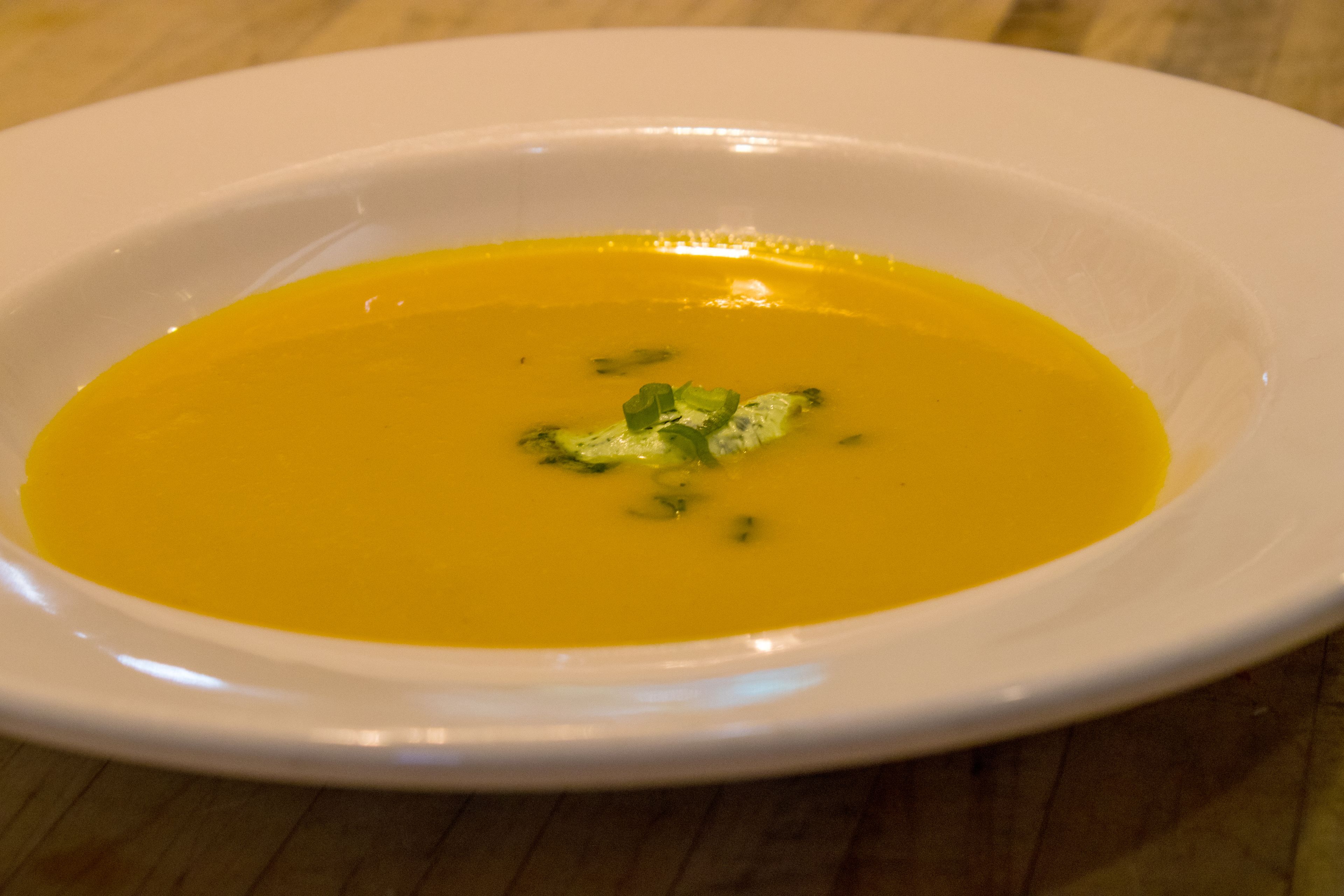 A white bowl of soup on a wooden table.